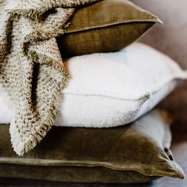A pile of cushions in shades of warm green and soft white, by Eadie Lifestyle