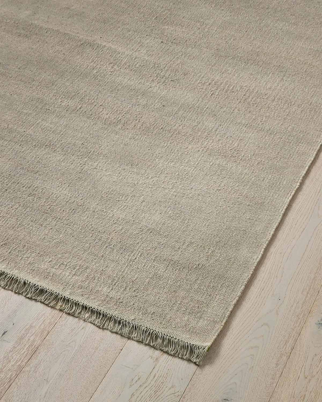 A cool taupe toned linen handwoven textural floor rug with fringed edges.