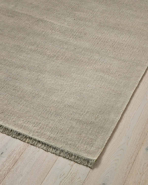 A cool taupe toned linen handwoven textural floor rug with fringed edges.