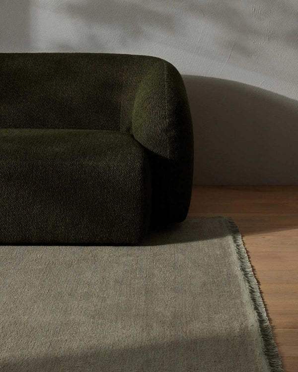 A modern style couch in deep green with a grey-green floor rug in 100% linen with fringed edges.
