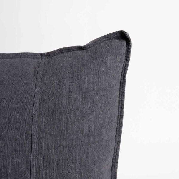 The corner of a linen cushion, with a delicate flange edge and hem detailing, in an on-trend navy colour.