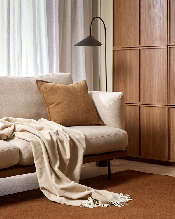 A cool light beige toned throw blanket in 100% merino wool, draped over a cream couch.