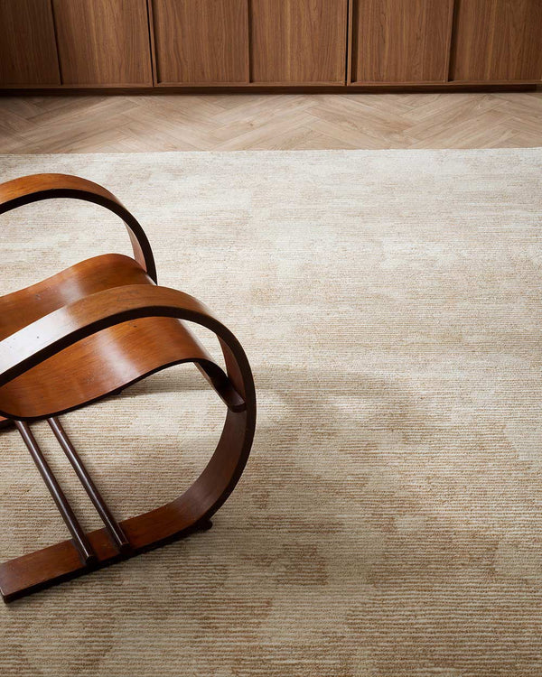 A designer chair on top of a beautiful New Zealand wool floor rug in shades of neutral cream and beige, with texturality through the cut and loop piling.