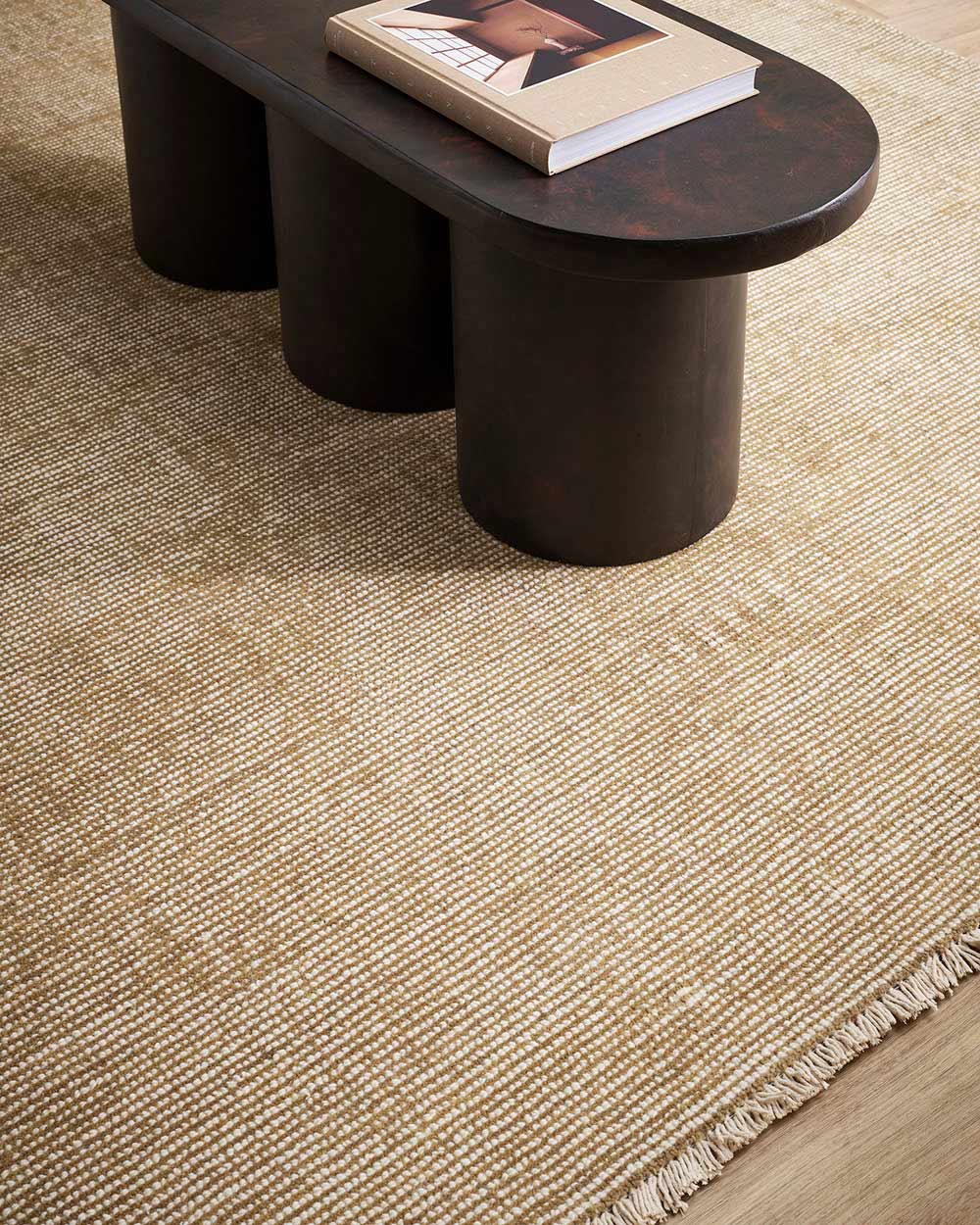A coffee table on a warm toned beige, lightly distressed 100% NZ wool floor rug with a subtle fringed edge.