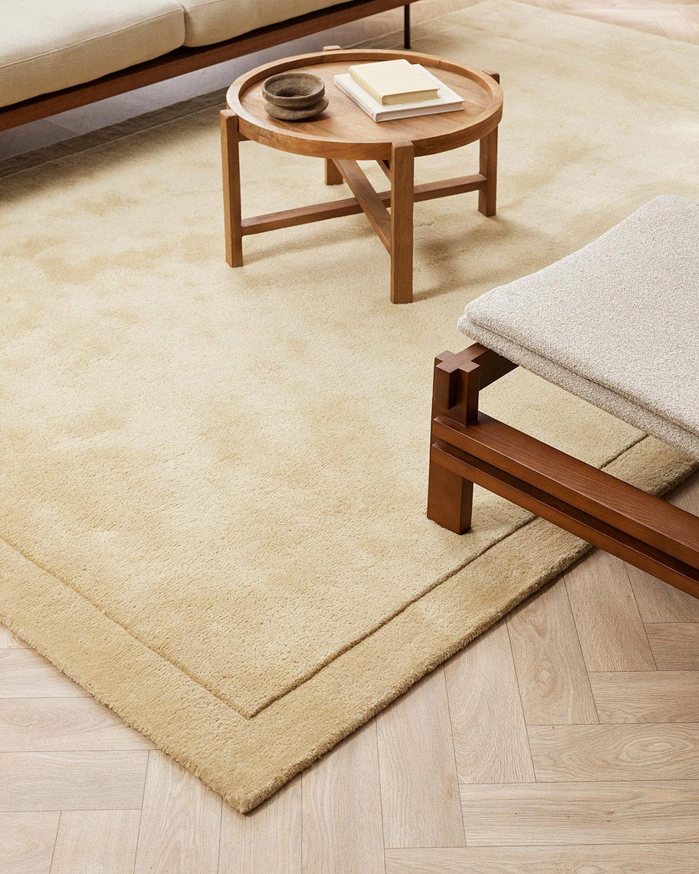 A floor rug with modern furniture in warm soft beige tones with cut pile frame detailing along the edges, in 100% NZ wool.