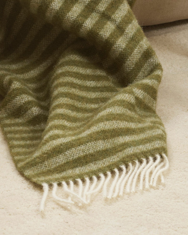 A detailed view of an olive and sage green striped throw blanket in 100% wool with soft cream twisted edging.