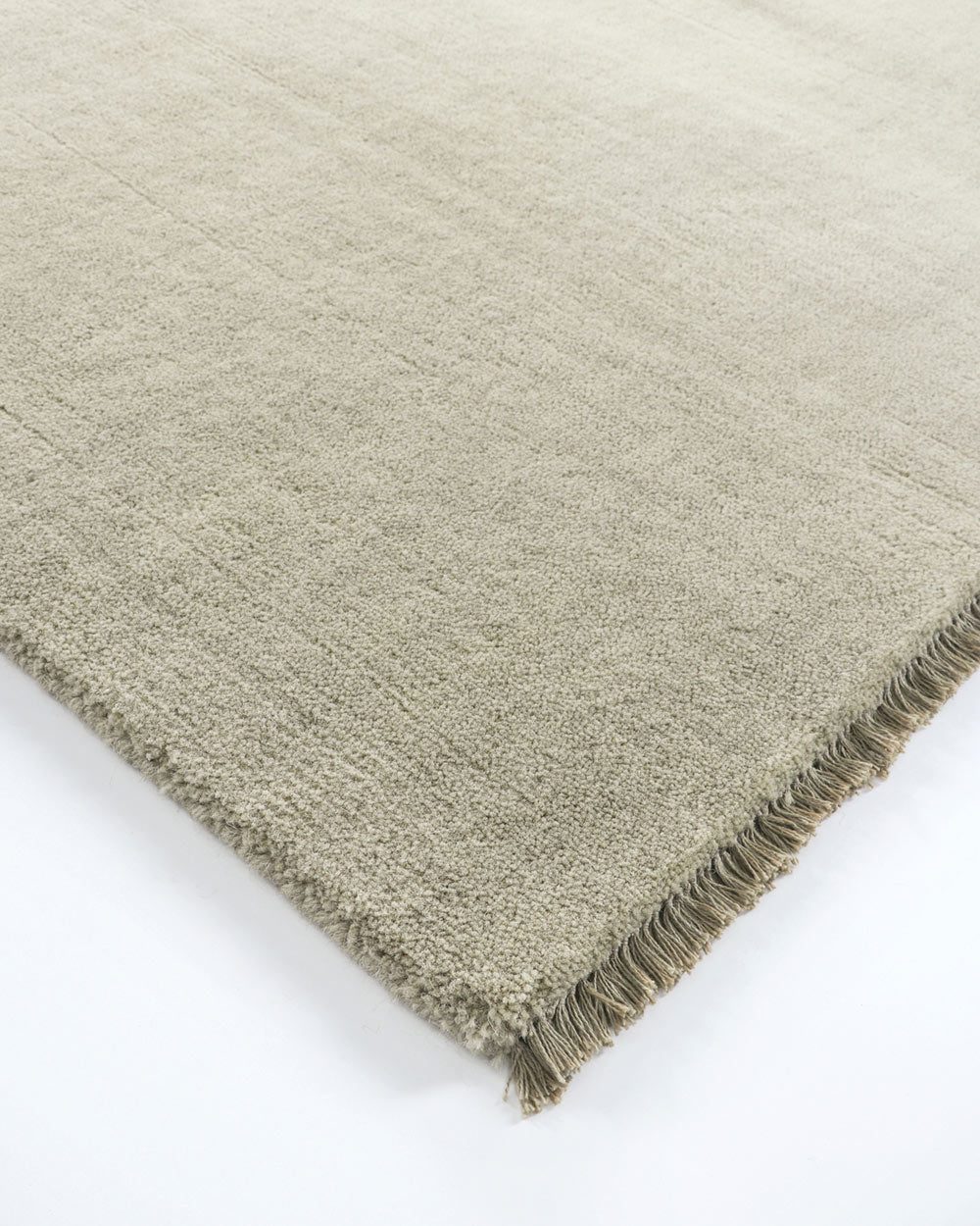 A corner image of a greige floor rug with fringed edges in 100% wool.