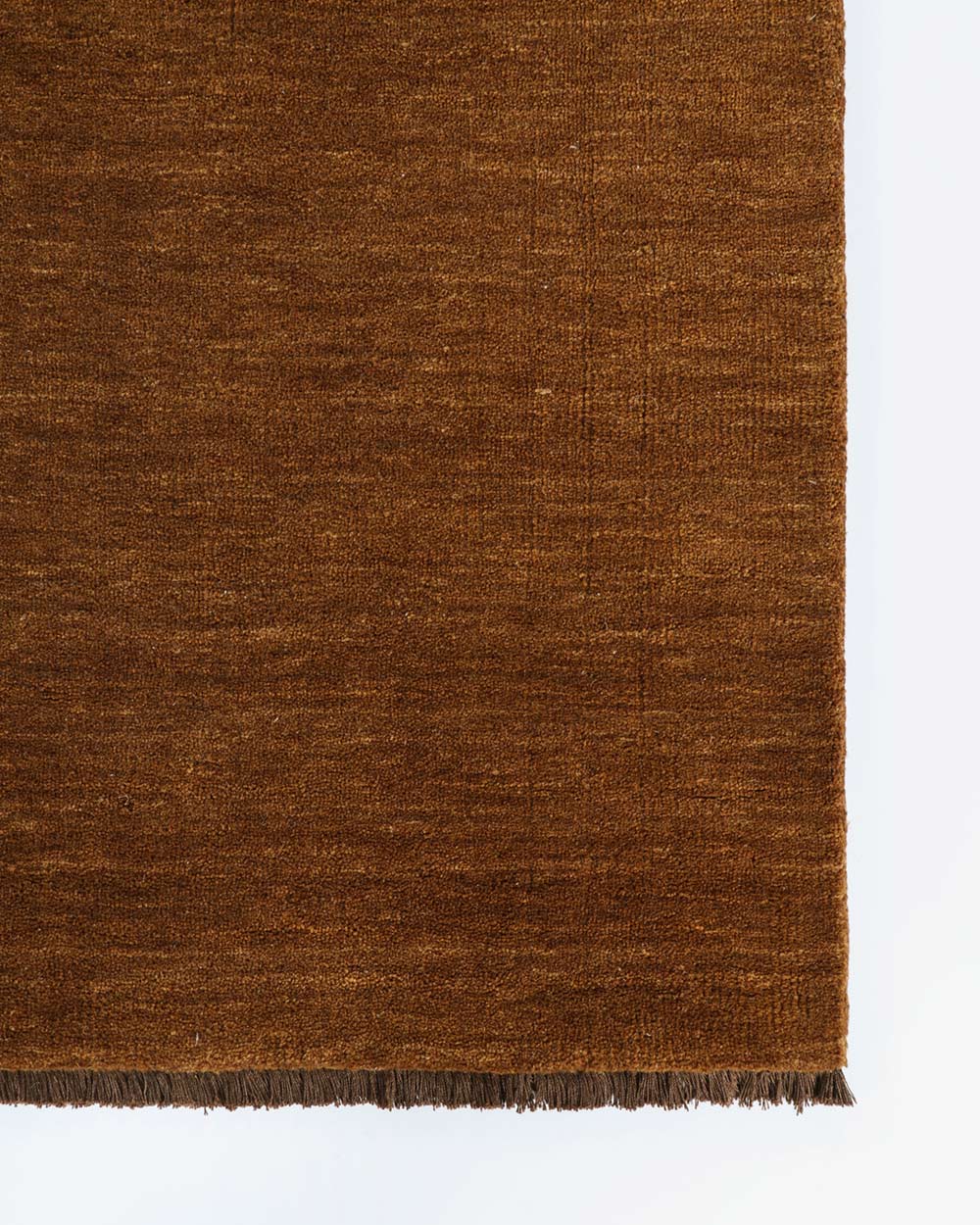 A corner image of a rich brown floor rug with fringed edges in 100% wool.