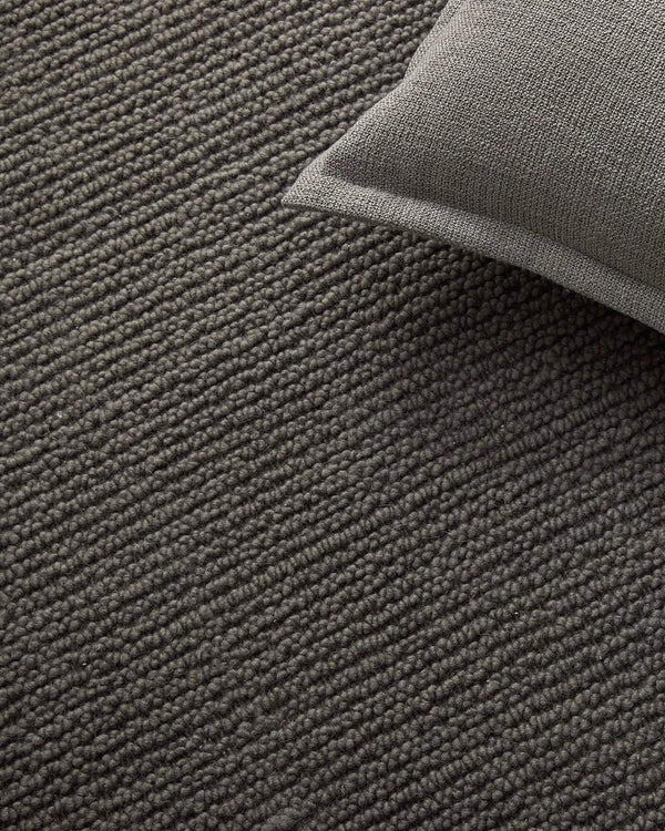 Gray textured rug with a corner of a gray pillow visible