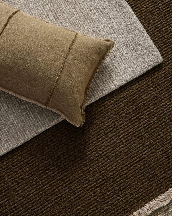 Textured green and beige rug with a pillow on top