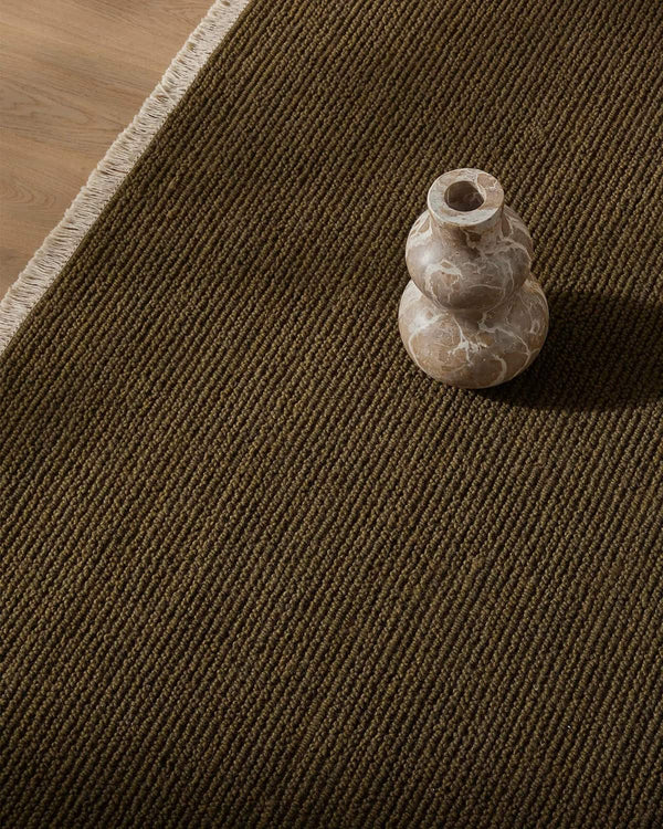 Small stone vase on a textured green-brown floor rug