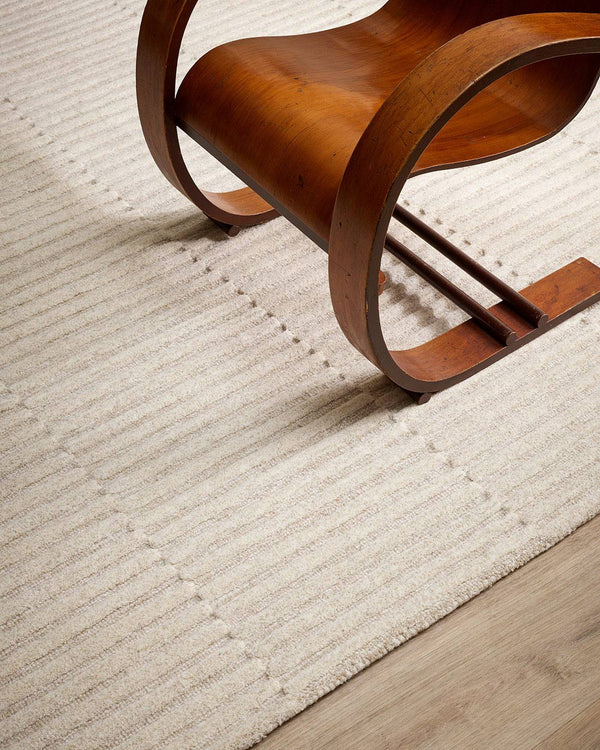 A modern style chair on a textured rug, with a linear pattern in a soft oatmeal shade. By Baya