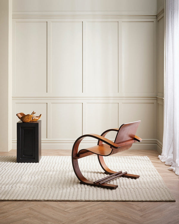 A stylish sitting room with a 100% wool floor rug in a linear striped cut and looped pile texture, in a soft cream neutral shade. By Baya