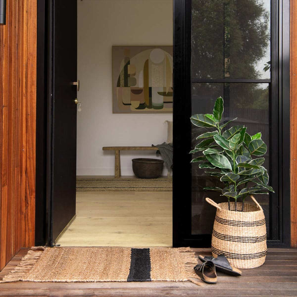 An open doorway with a natural toned doormat made of knotted jute, with a black asymmetrical stripe.