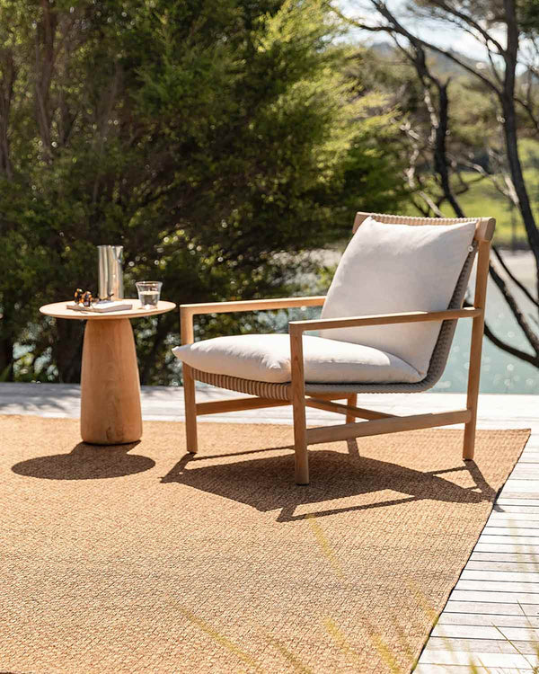 A brown, basketweave outdoor rug by Baya NZ, sitting on a sunny deck with a chair and table.