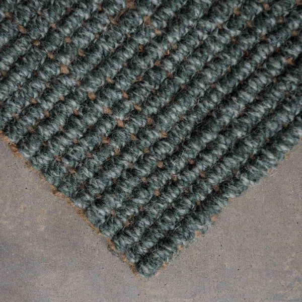 A close up of the corner of a muted forest green boucle weave wool and jute floor rug.