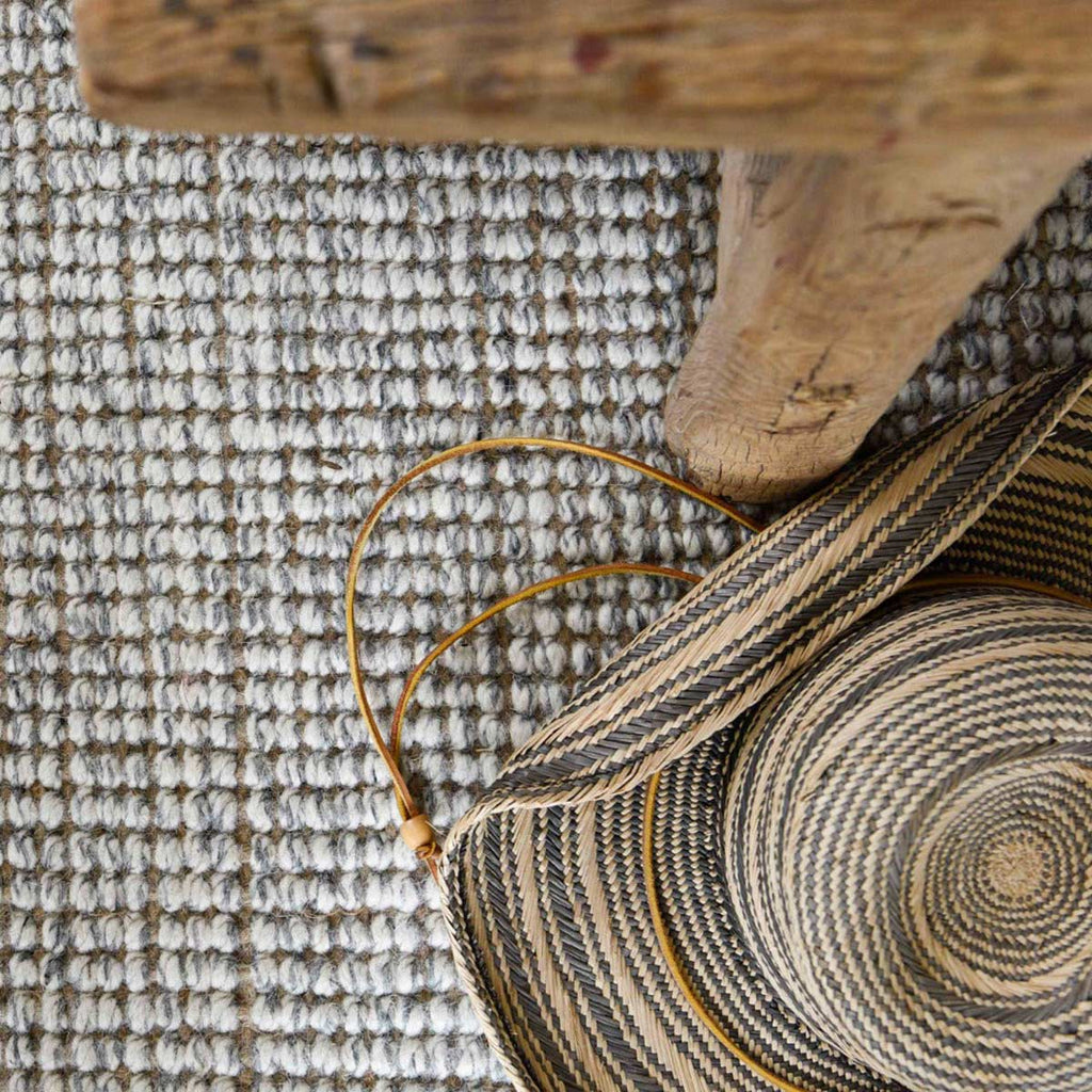 A close up of a boucle style floor rug, made with a blend of white and grey wool and natural jute.