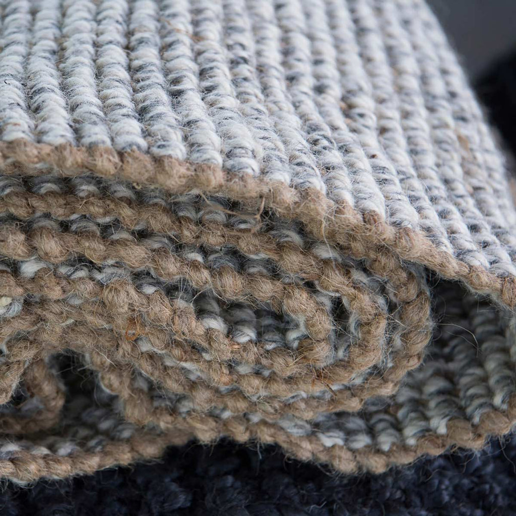 A rolled up floor rug, the edges made with natural brown jute and interspersed with cream and grey wool.