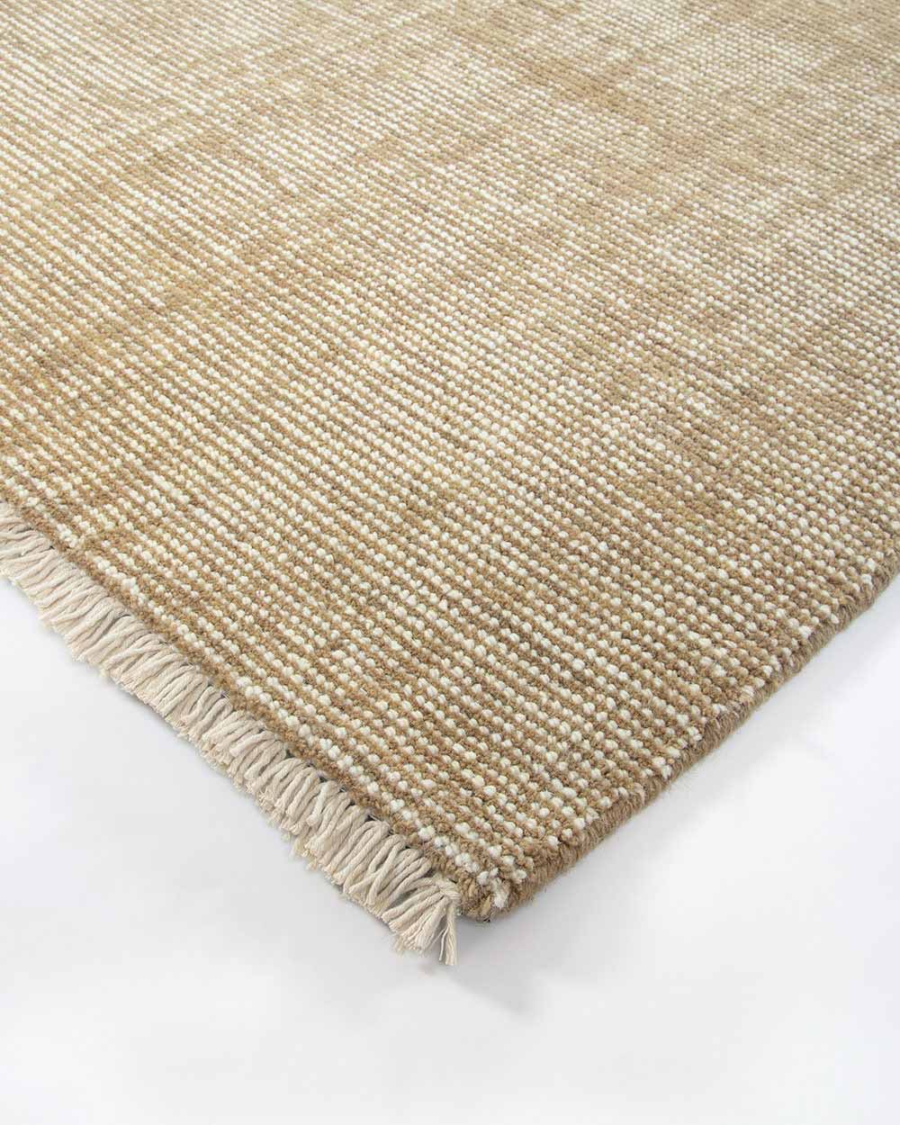A corner image of the Corbett floor rug in the shade Honey, a lightly distressed contemporary warm beige, with cream detailing and a short creamy fringe. By Baya