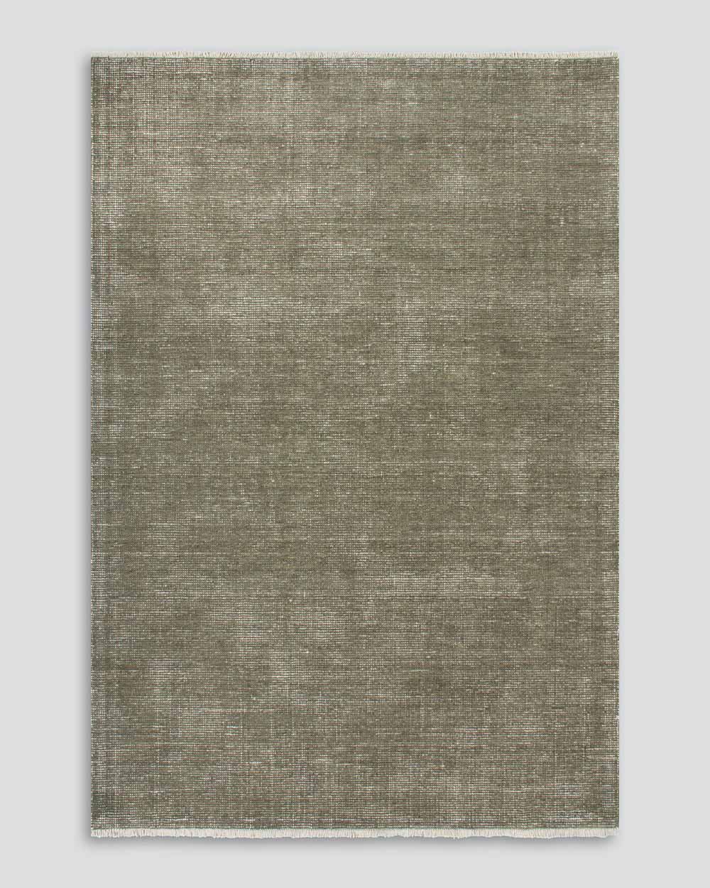 A full image from above of the Corbett floor rug in the shade Lichen, a lightly distressed contemporary warm green, with cream detailing and a short creamy fringe. By Baya