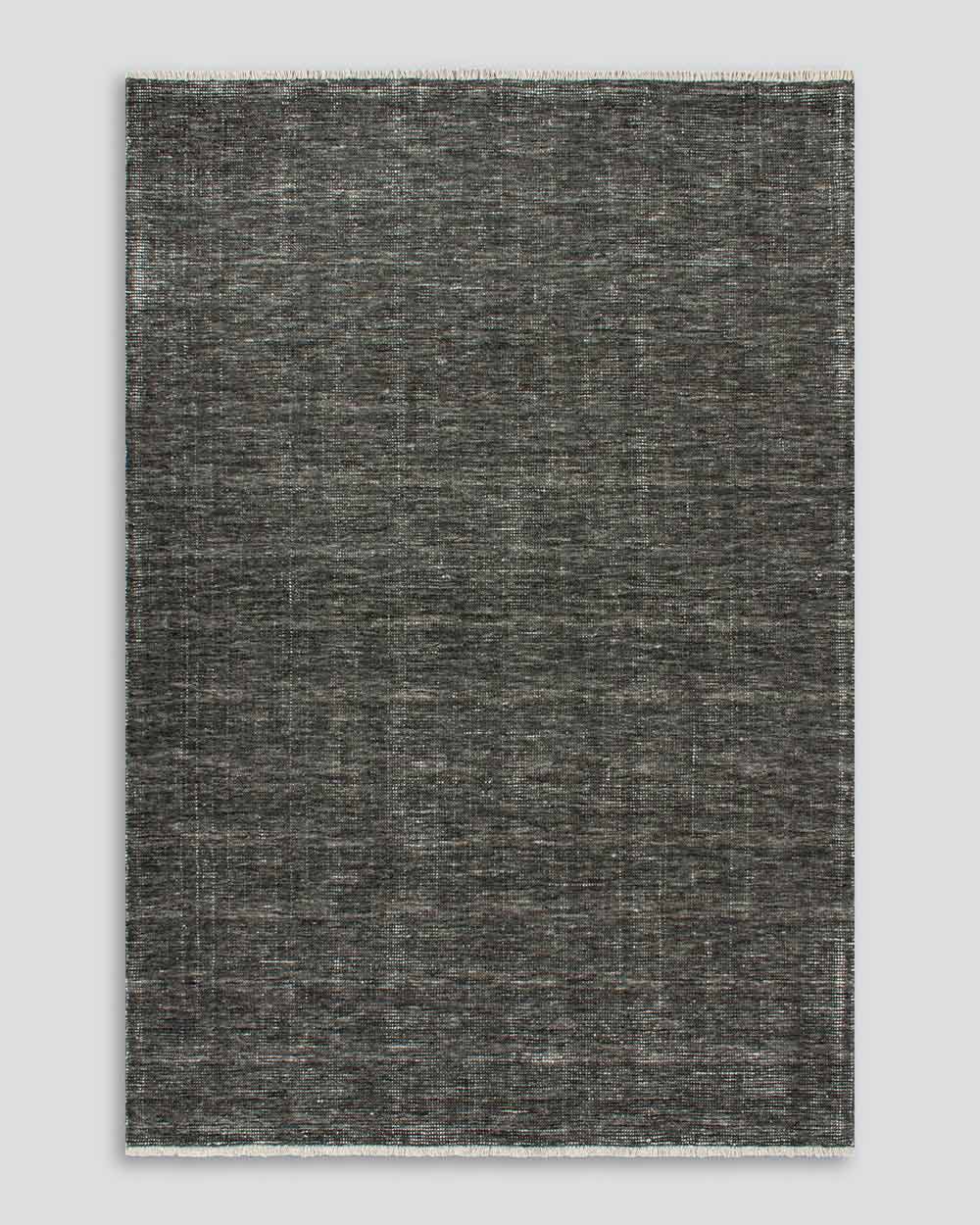 A full image from above of the Corbett floor rug in the shade Peat, a lightly distressed contemporary soft charcoal, with cream detailing and a short creamy fringe. By Baya