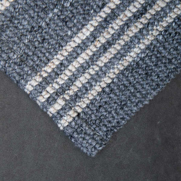 A corner view of a slate grey mat with natural toned stripes, made from 100% recycled PET.