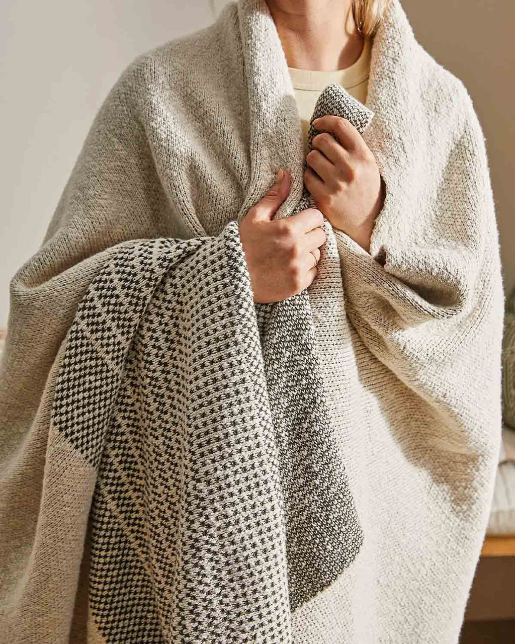 A woman wrapped up very cozy in Weave Home's double edged cotton knit throw in Sonoma.
