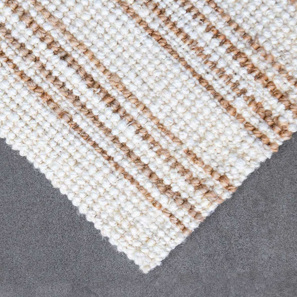 A close up image of the corner of a white washed and natural jute striped floor rug.