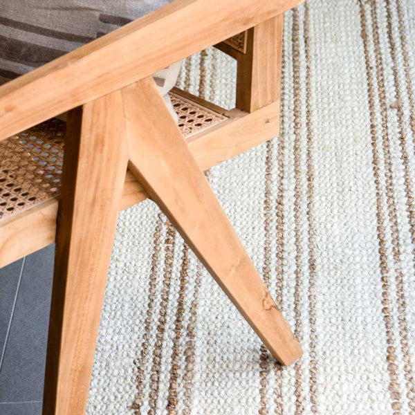 A close up image of a chair on top of a striped, white-washed and natural jute rug.