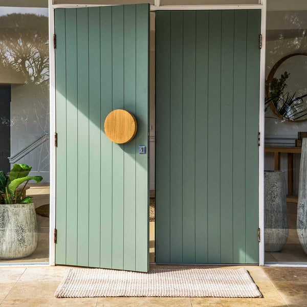 A modern double door with an oversized entrance mat made with recycled materials in a neutral beige tone with crisp white stripes.