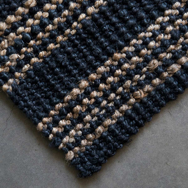 The corner of a handknotted jute floor rug in graphite, with natural brown stripes.