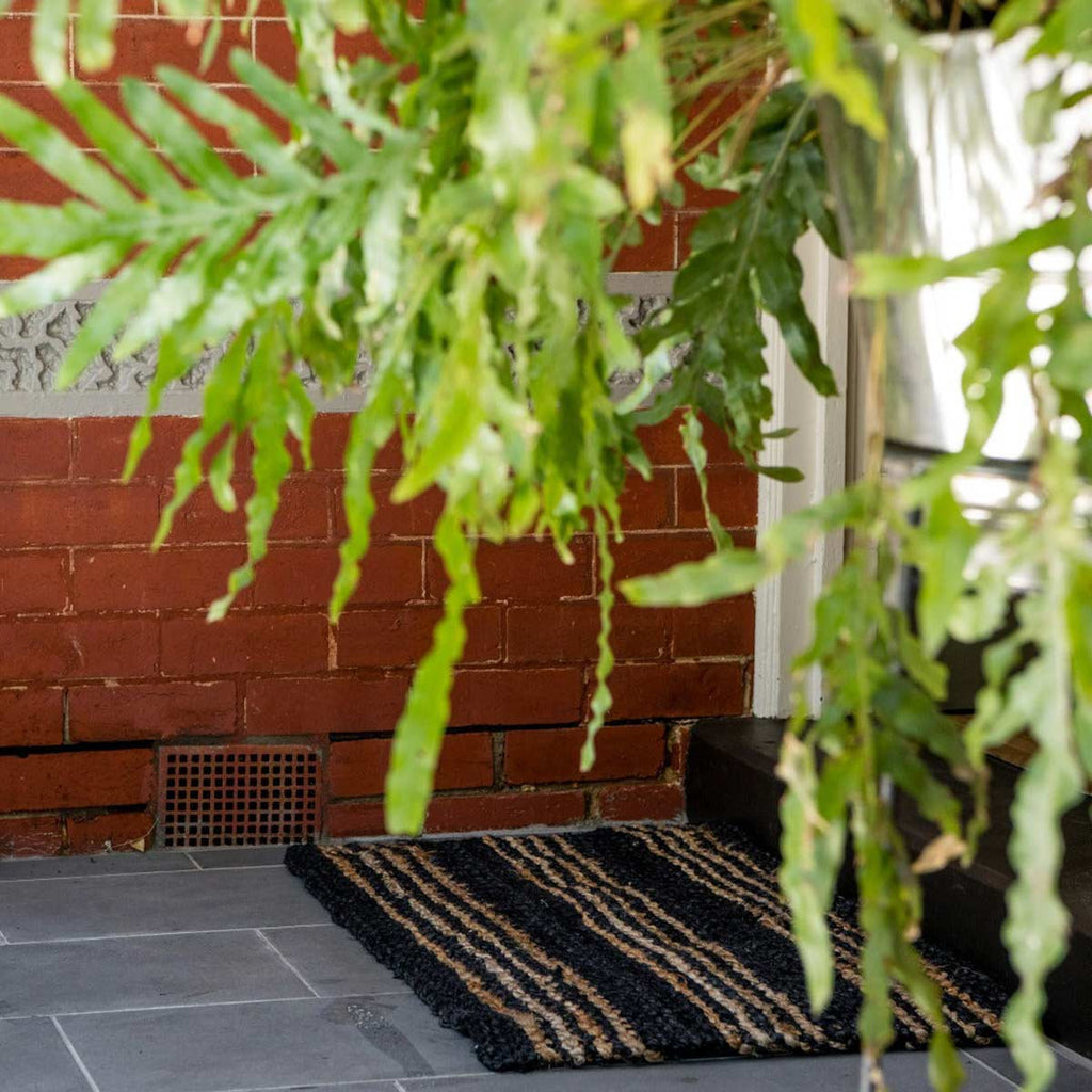 A doormat made of natural jute with brown and black stripes.