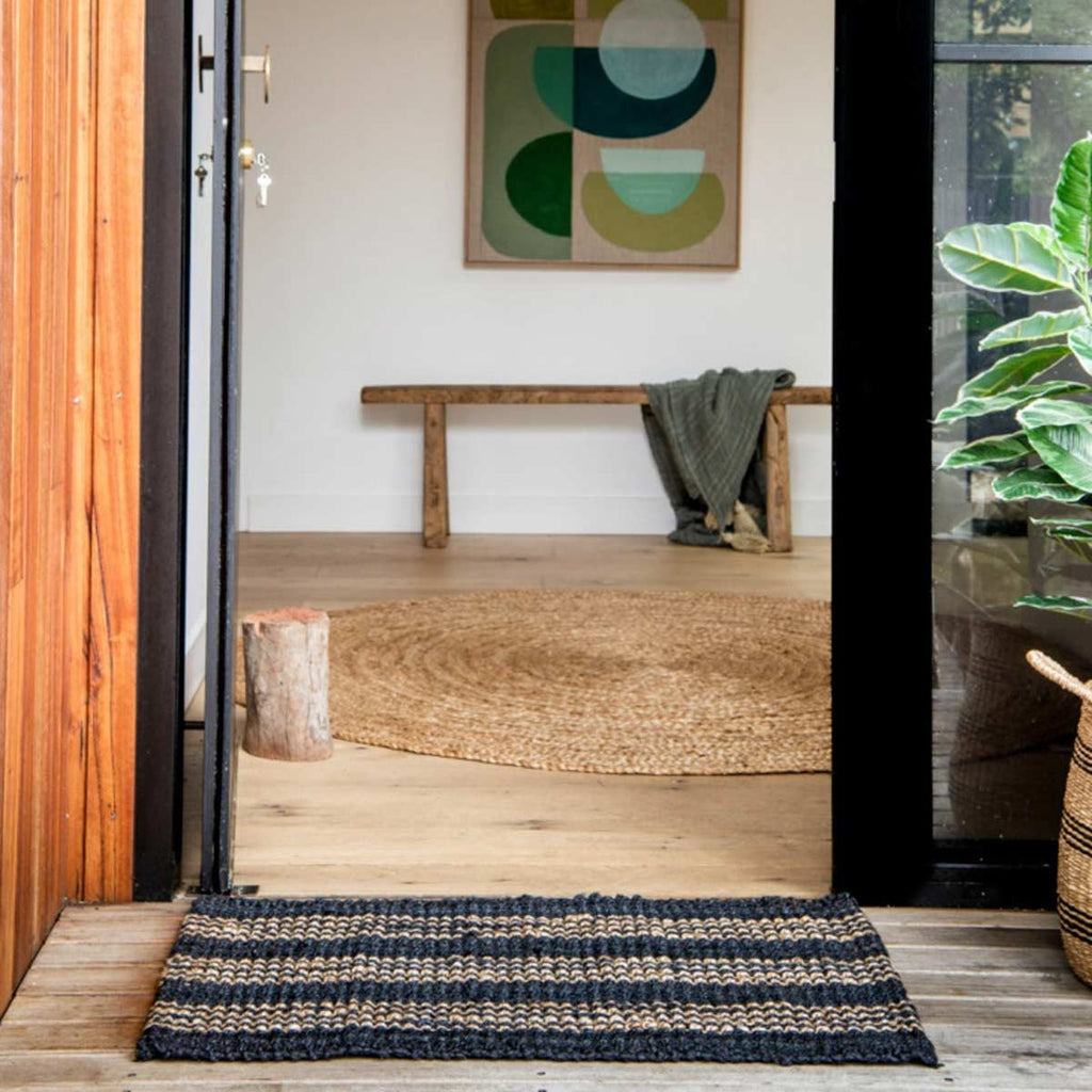 An entranceway with a black jute doormat with natural brown striping.