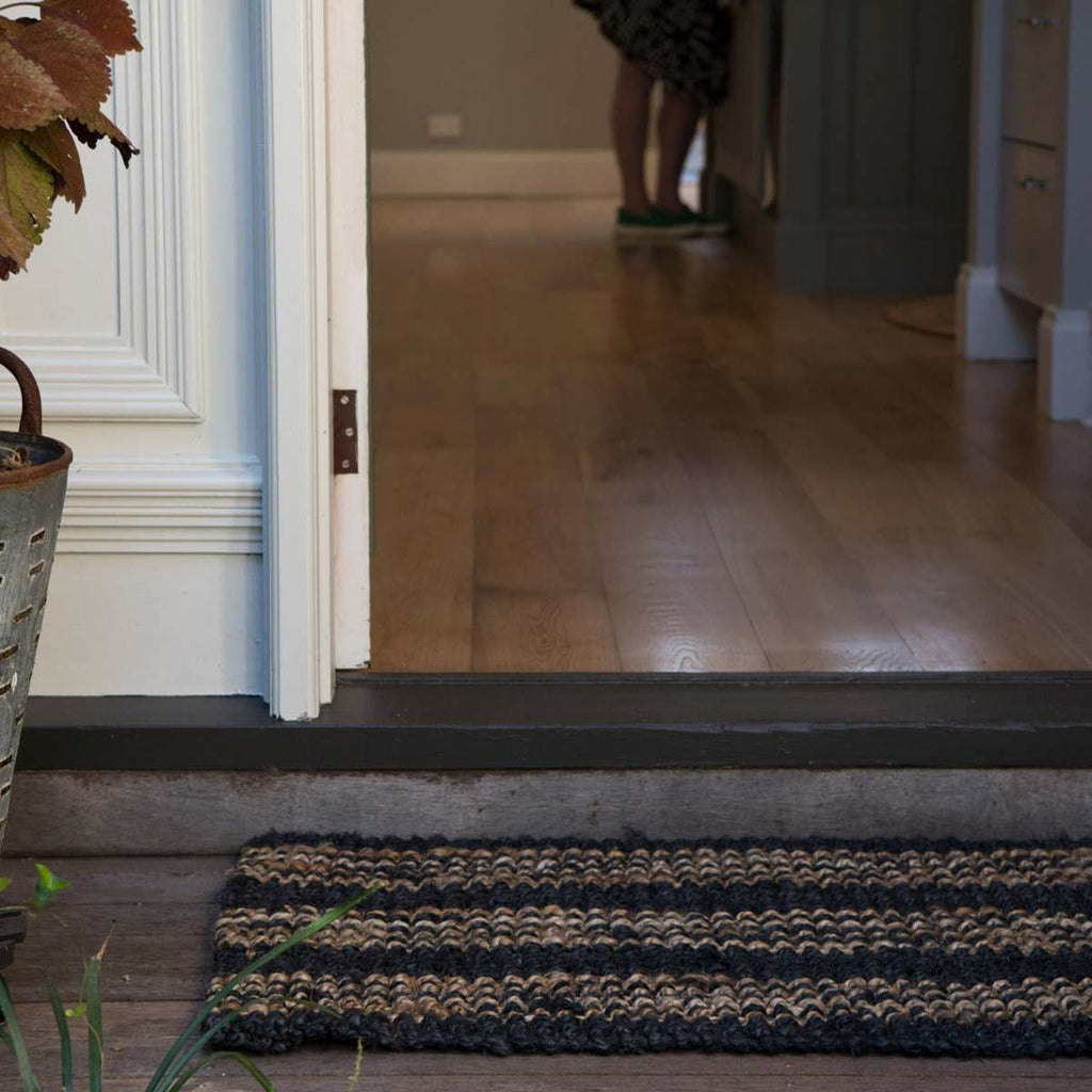 An entrance way with a black and brown striped doormat made with hand knotted jute.