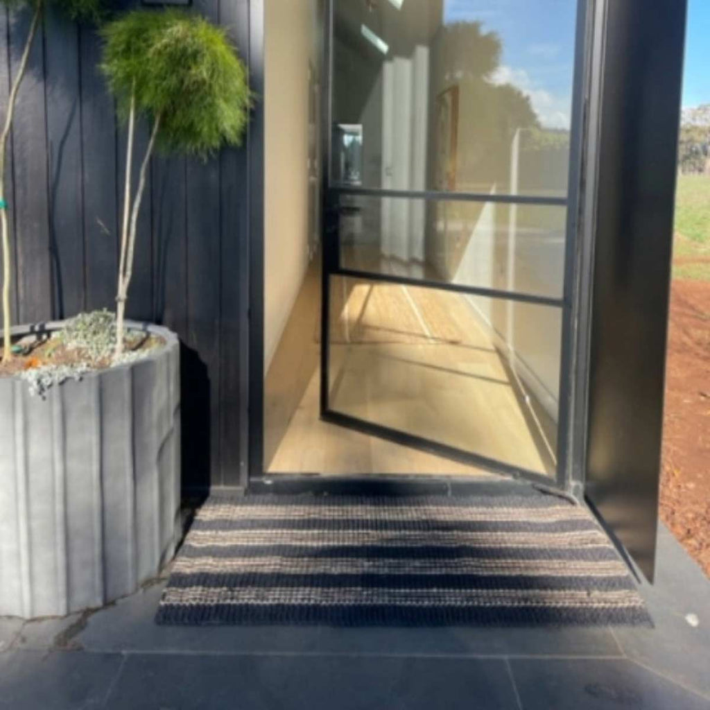 A doorway with an oversized jute doormat in black and natural stripes.