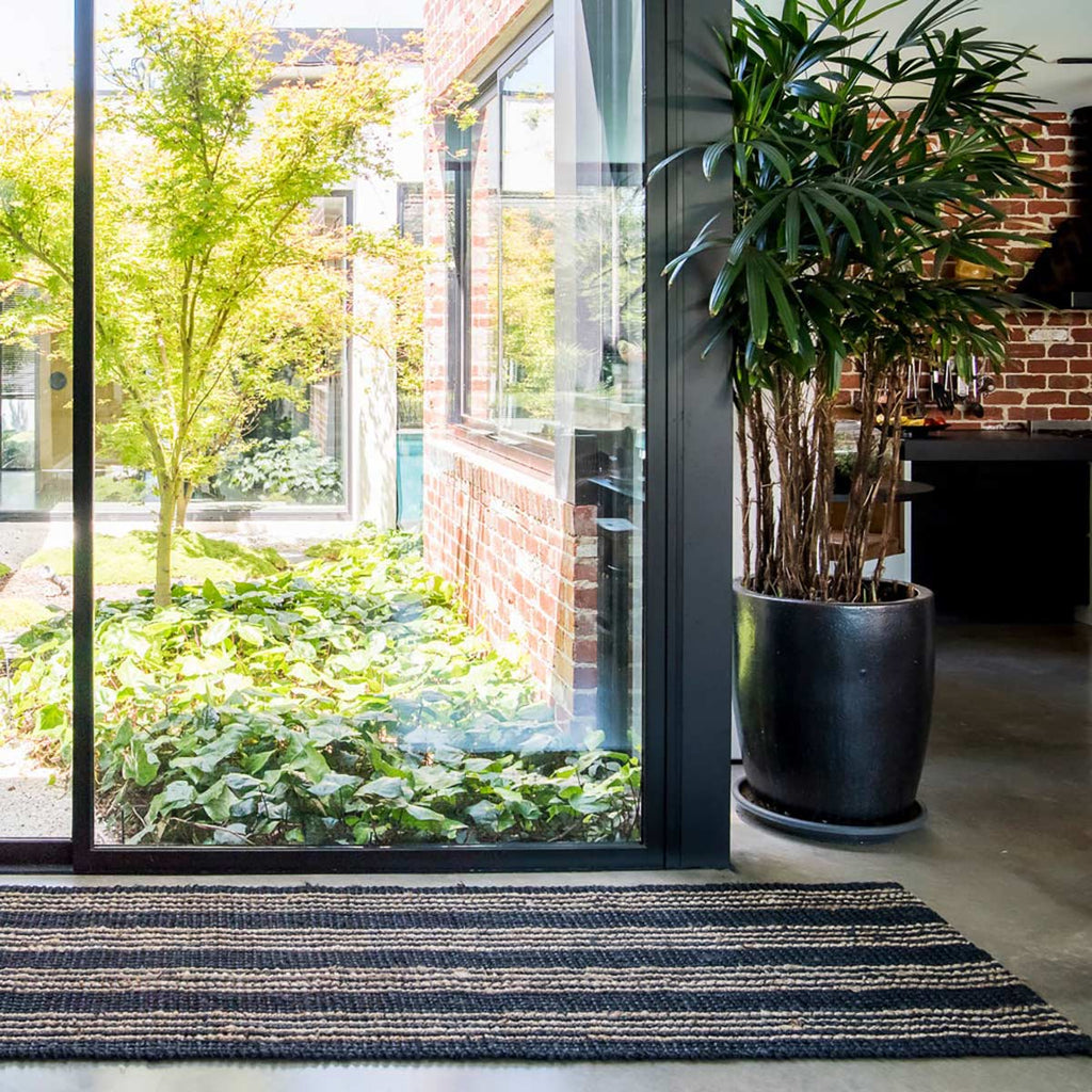 A doorway with a long runner as an entrance mat, patterned with graphite and natural brown stripes and handwoven out of jute fibres.
