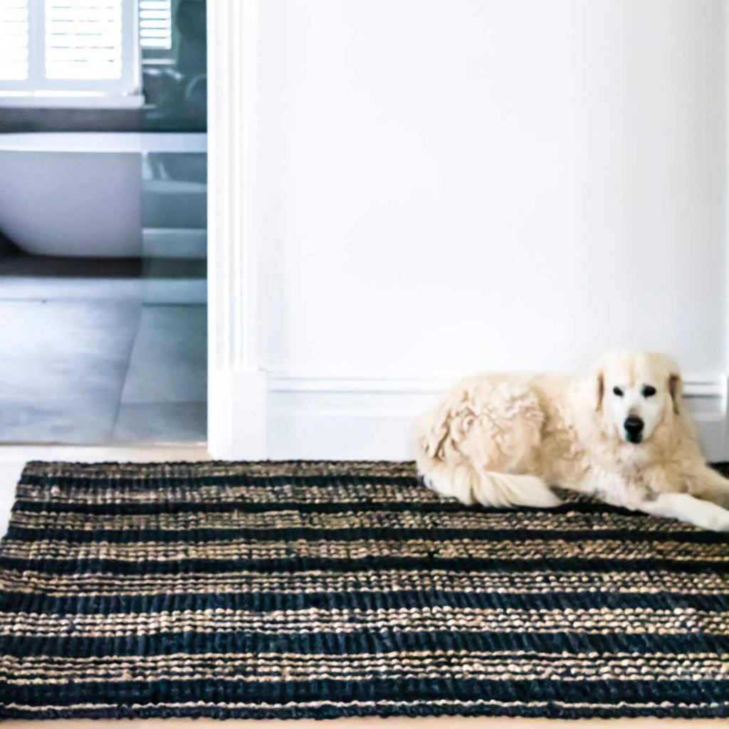 A dog lying on a floor rug made of deep navy blue jute fibres with natural brown striping.