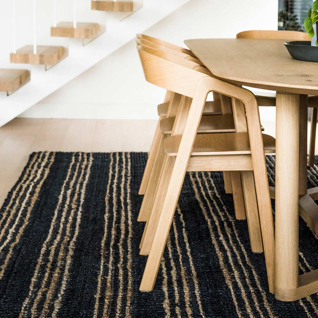 A modern style dining room with a hand knotted bohemian style black floor rug with natural brown striping, made with 100% natural jute fibres.