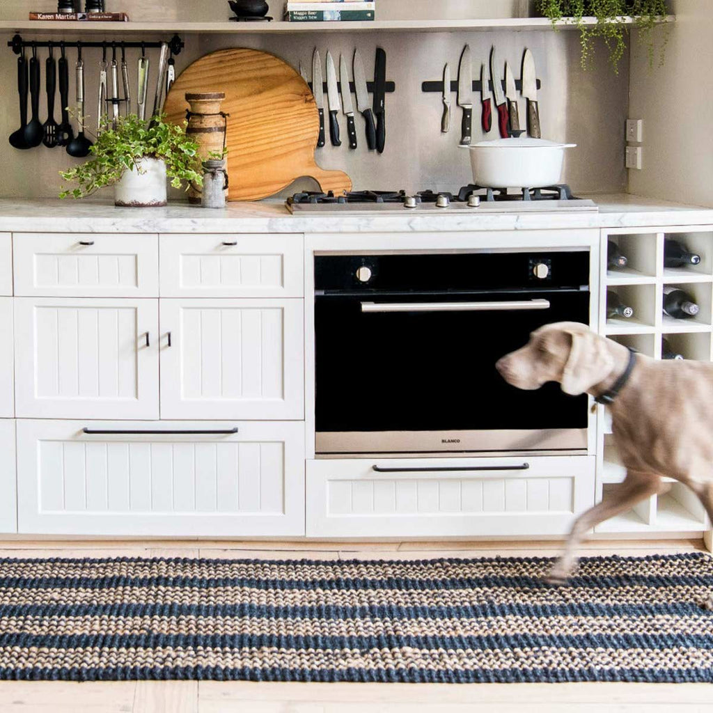 A dog runs along a kitchen runner, made of jute and with a black and brown striping pattern.