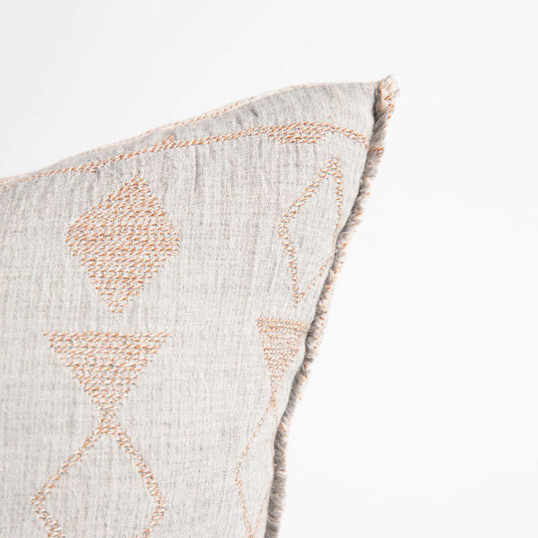 A corner view of a patterned cushion, with pale blue and soft clay tones in a geometric pattern, and a softly fringed edge.