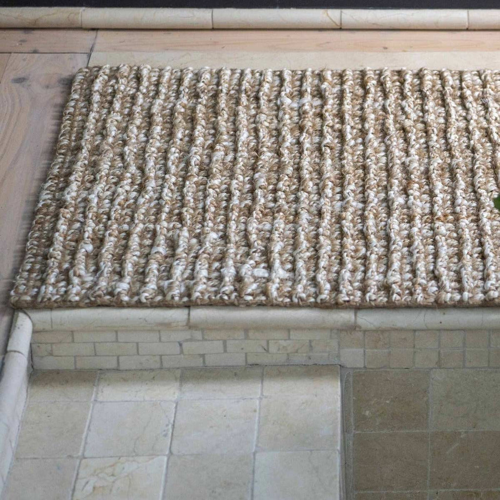 A floor mat made of jute, textured with a hand knotted stripe, in natural brown and white fibres.