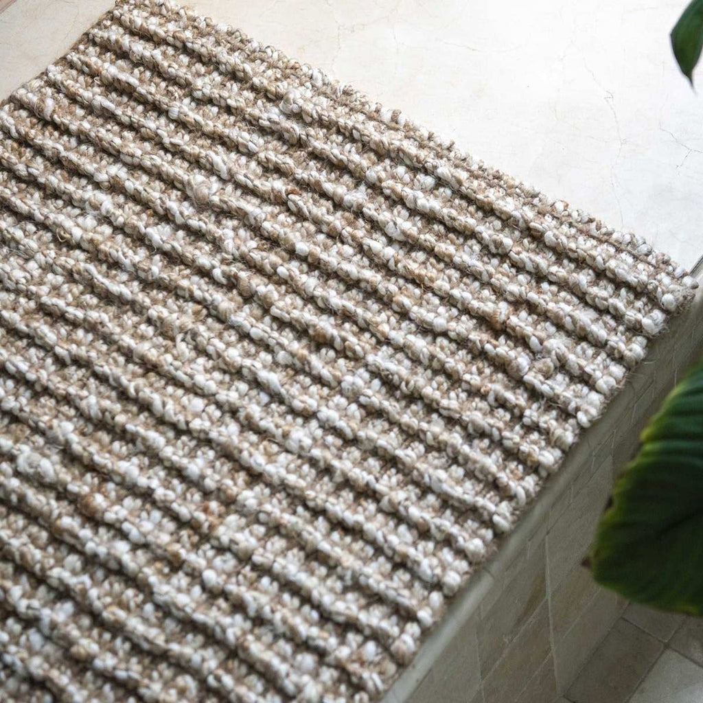 The edge of a textural hand made floor mat made with natural and white washed jute fibres.