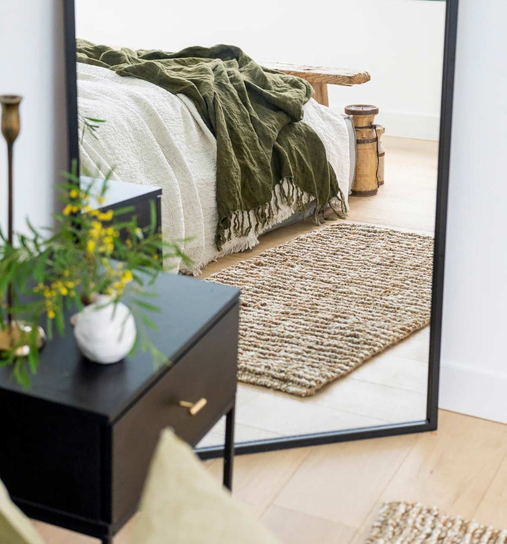 An oversized natural brown and white textured jute floor mat next to a bed.