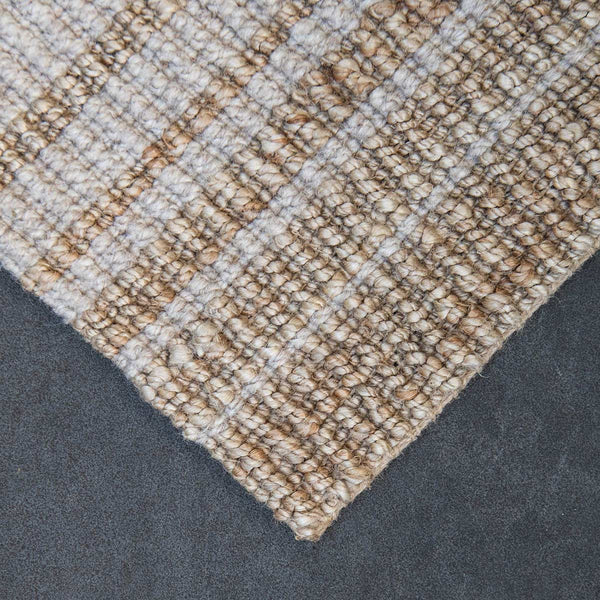 The corner of a striped wool and jute floor rug, in natural brown and white tones.
