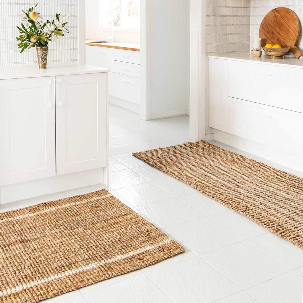 An entryway with two jute floor mats, both in natural jute fibres with one subtly striped in white wool and one more boldly with whitewashed jute.