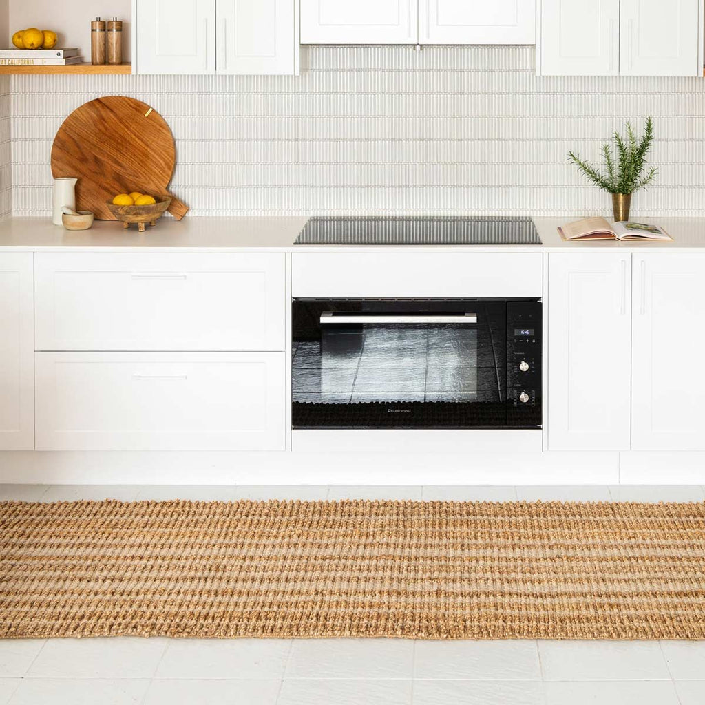 A white minimalist kitchen with a striped floor runner in textured hand knotted jute and wool fibres.