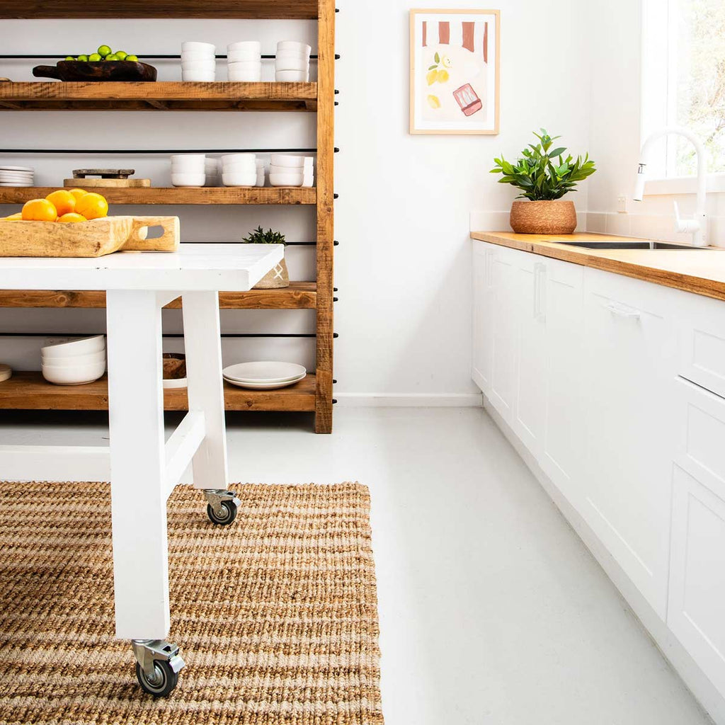 A striped floor rug under a kitchen table, in hand knotted jute and wool fibres.