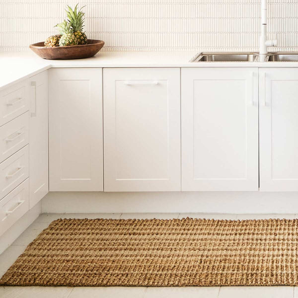 A white toned kitchen with a subtly striped kitchen runner in wool and natural jute tones.