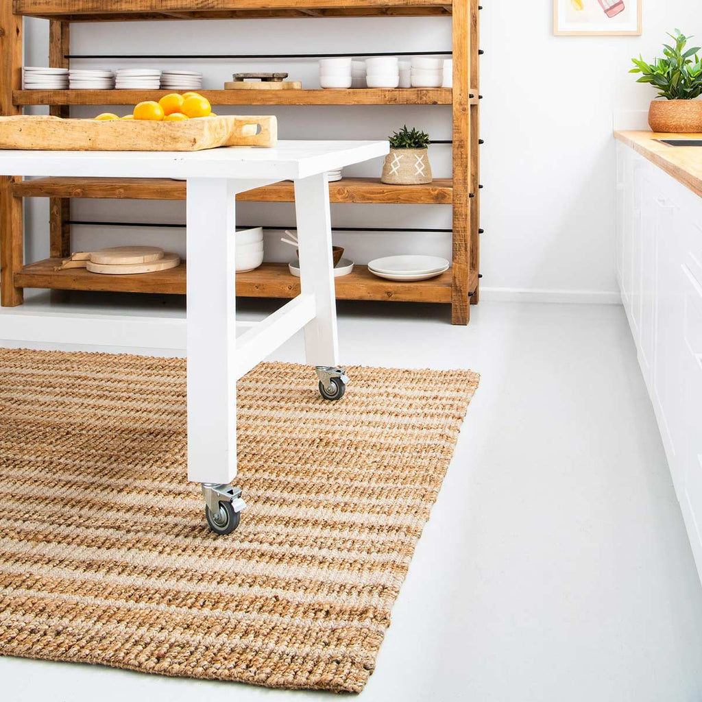A kitchen table on top of a natural brown and off-white striped floor rug made of jute and wool.