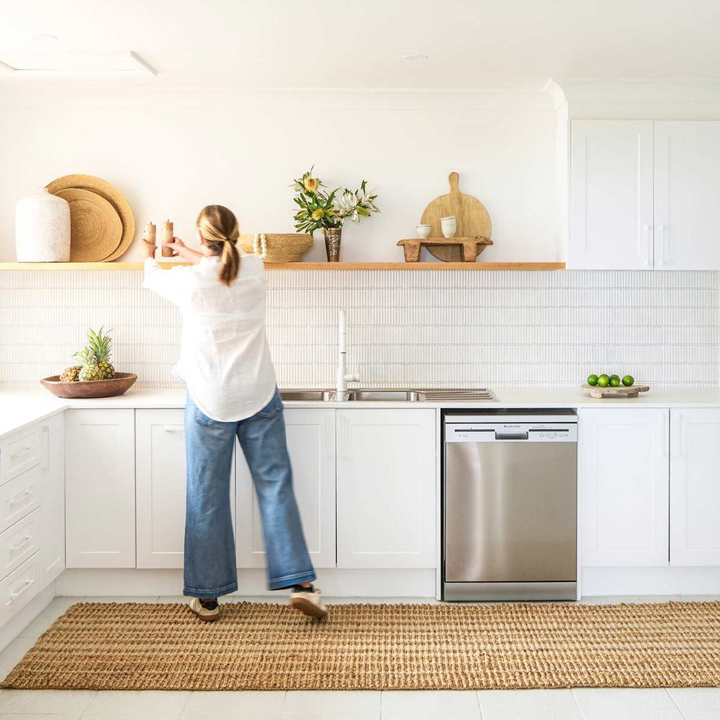 A woman in a white kitchen, with a striped floor runner in wool and jute.